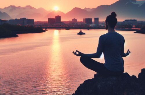 L’immagine che hai inviato mostra una persona seduta su una roccia in posizione meditativa con lo sfondo di un tramonto su un corpo d’acqua, forse un fiume o un lago, con montagne e edifici silhouettati contro il cielo arancione. La scena trasmette una sensazione di tranquillità e potrebbe essere rilevante per argomenti legati alla meditazione, al benessere o alla natura